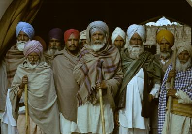 Un groupe d'homme se tient debout, ils sont vêtus de turbans colorés et de grands châles par dessus une tenue traditionnelle
