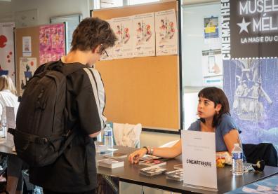 Un étudiant échange avec une dame assise à un Stan qui présente la Cinémathèque