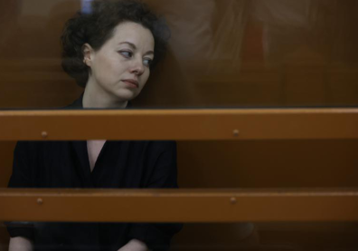 Femme brune assise derrière des barreaux et regardant vers sa gauche