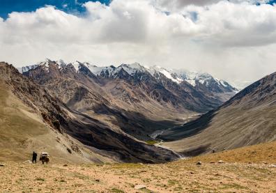 Vue entre deux chaînes de montagnes, un ruisseau au milieu, les pics de montagnes enneigés et un ciel blanc de nuages 