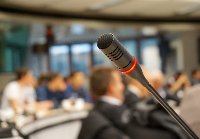 Photo d'un microphone au premier plan avec en arrière plan des personnes floues