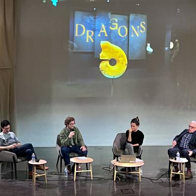 A stage on which 4 people are sitting with microphones in hand, talking to each other.