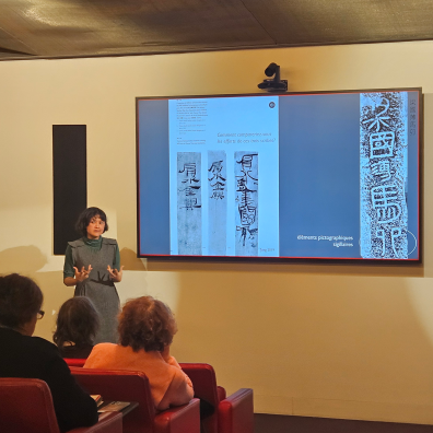 Une enseignante parle dans un auditorium avec un écran derrière pour illustrer 