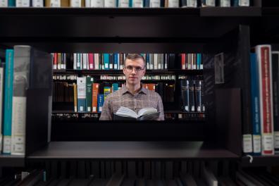 Jeune homme avec des lunettes en train de lire un livre dans une bibliothèque