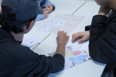 Des étudiants de dos sont assis entrain de travailler sur un bureau avec des documents