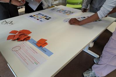Plusieurs personnes sont autour d'une table sur laquel le sont posés des feuilles et morceaux de papier en couleur