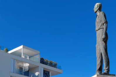 Une statue d'un homme qui regarde le haut d'un immeuble avec un ciel bleu