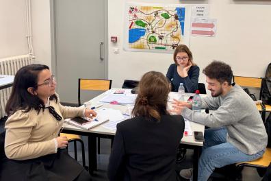 Groupe d'étudiants discutant autour d'une table, une carte est accrochée sur le mur derrière eux