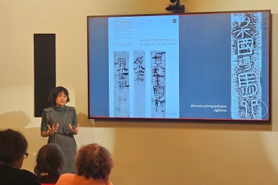 Une enseignante parle dans un auditorium avec un écran derrière pour illustrer 