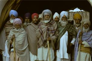 Un groupe d'homme se tient debout, ils sont vêtus de turbans colorés et de grands châles par dessus une tenue traditionnelle