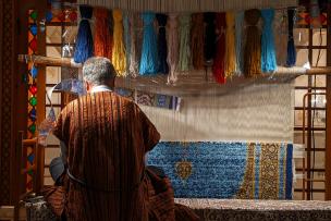 Un homme assis de dos tisse un tapis