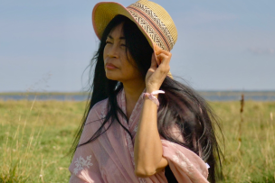 Portrait d'une femme dans un champ, elle porte sa main à son chapeau 