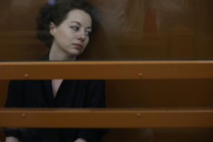 Femme brune assise derrière des barreaux et regardant vers sa gauche