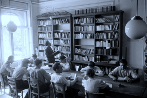 Photo en noir et blanc de personnes assis autour d'une table rectangulaire avec en arrière plan une bibliothèque