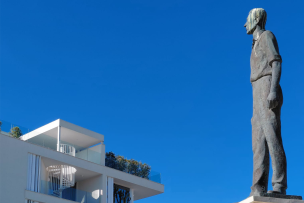 Une statue d'un homme qui regarde le haut d'un immeuble avec un ciel bleu