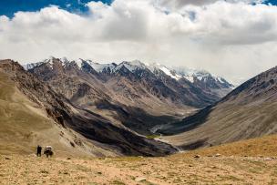Vue entre deux chaînes de montagnes, un ruisseau au milieu, les pics de montagnes enneigés et un ciel blanc de nuages 