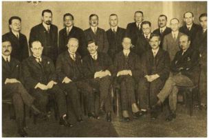 Photo en noir et blanc d'hommes en costumes noires assis et debout