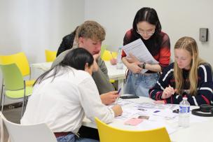 Students are sitting around a table, working. 